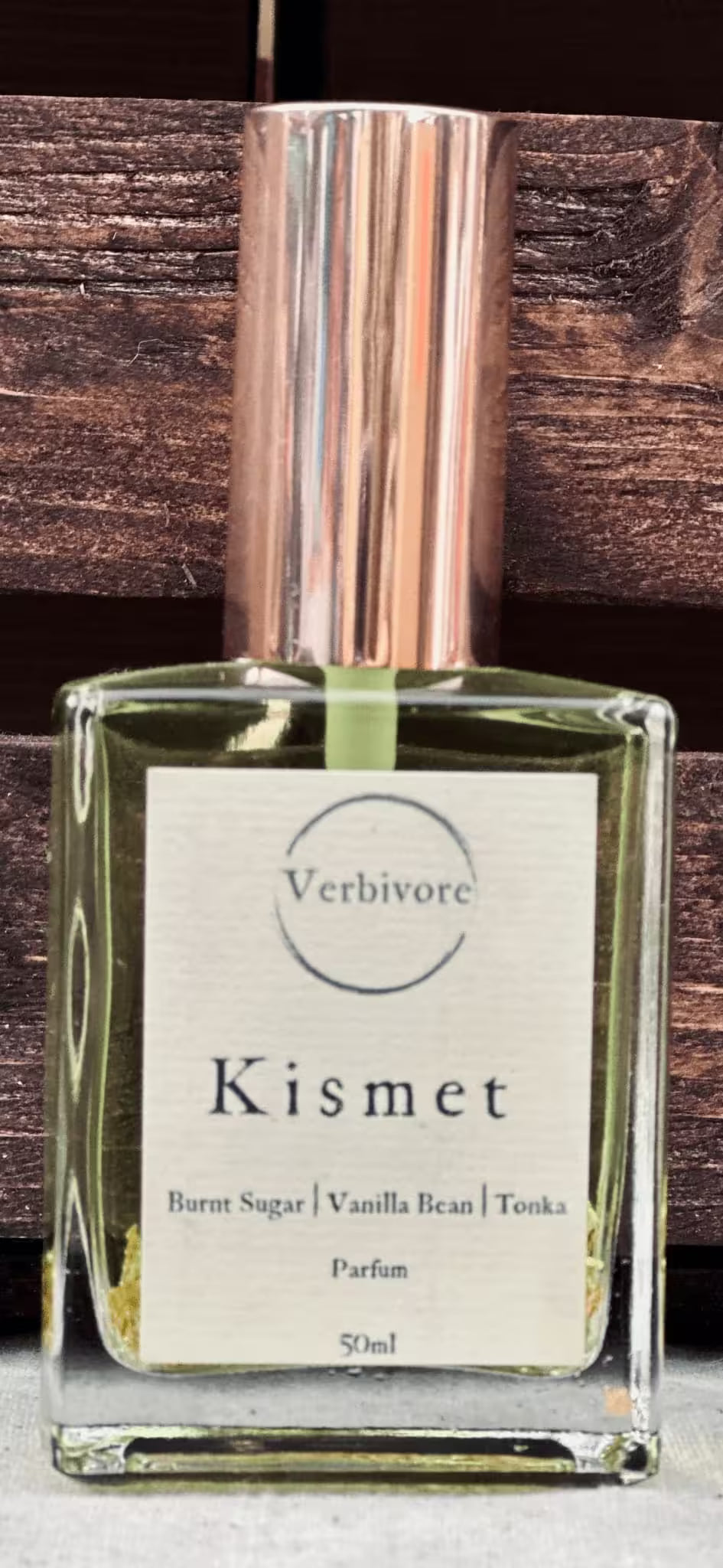 Perfume bottle labeled 'Kismet' by Verbivore with a wooden background