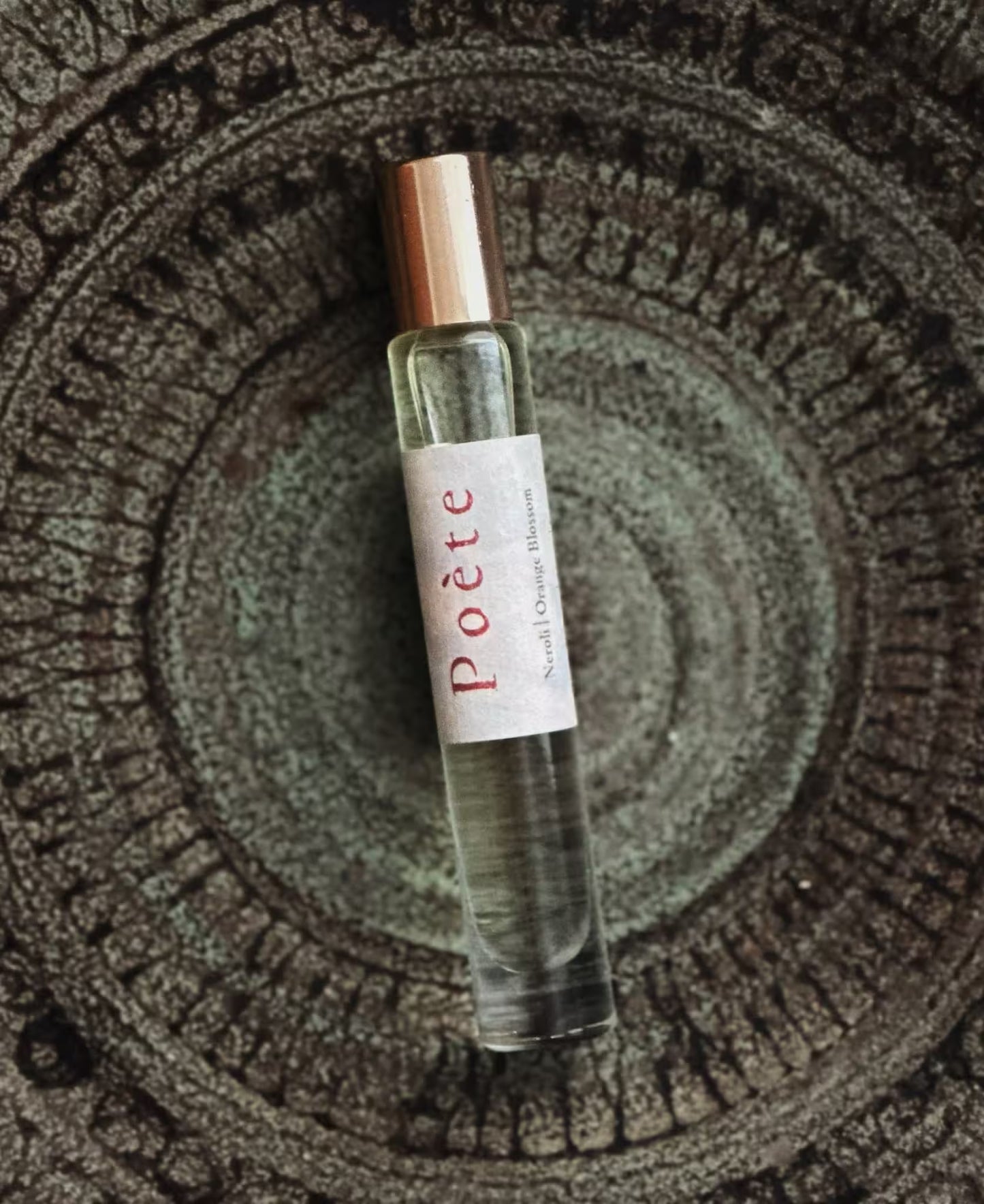 Roll-on perfume bottle labeled 'Poète' on a textured surface