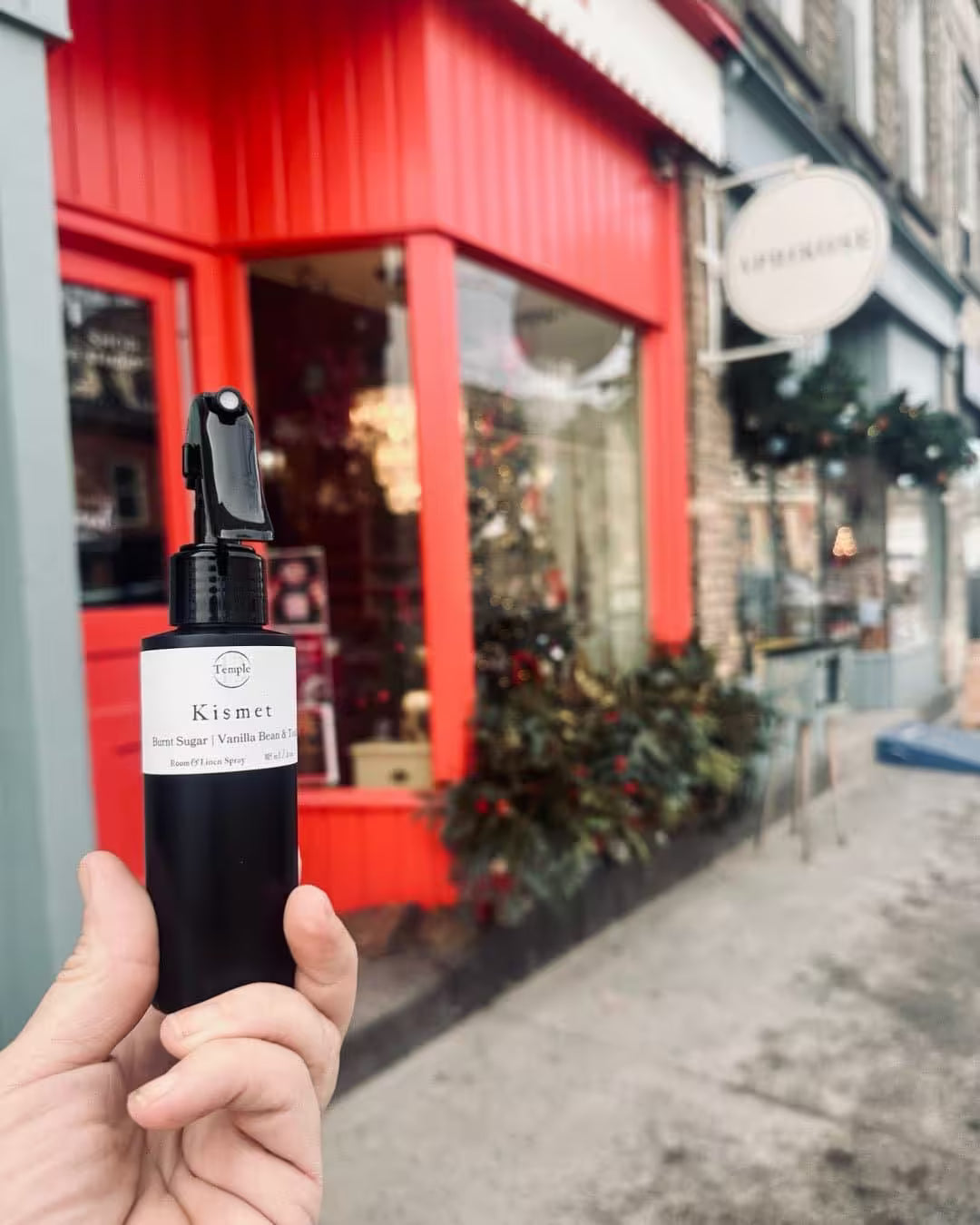 Hand holding a black spray bottle with a red building in the background