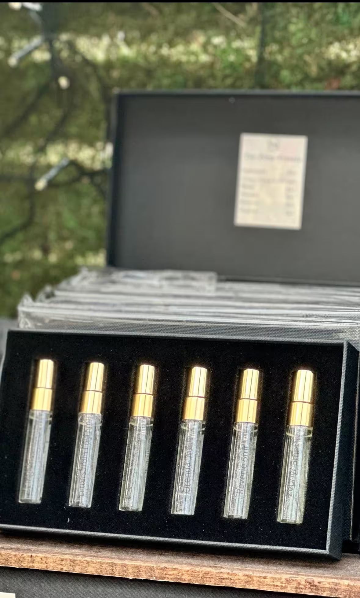 Set of six perfume bottles in a black case with a blurred outdoor background