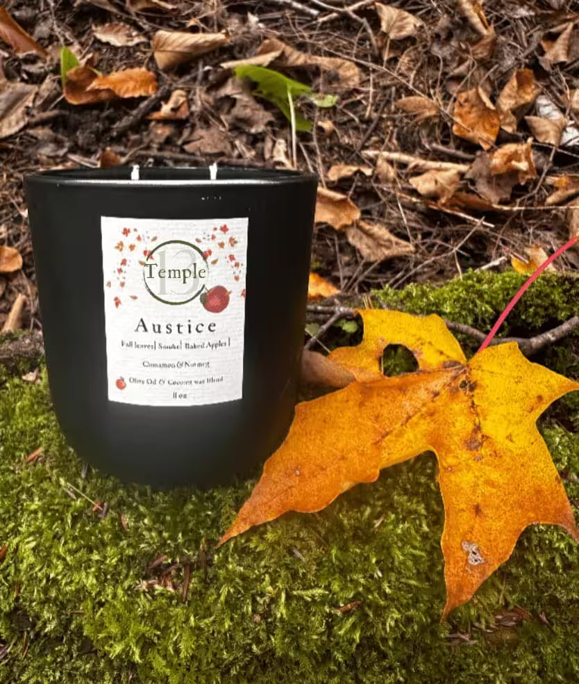 Black candle with a label on a forest floor with leaves and moss