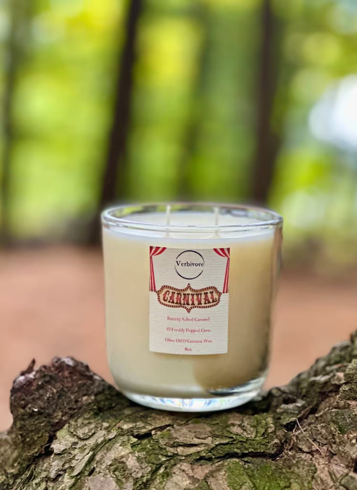 Candle in a glass jar with a label on a tree stump in a forest setting.