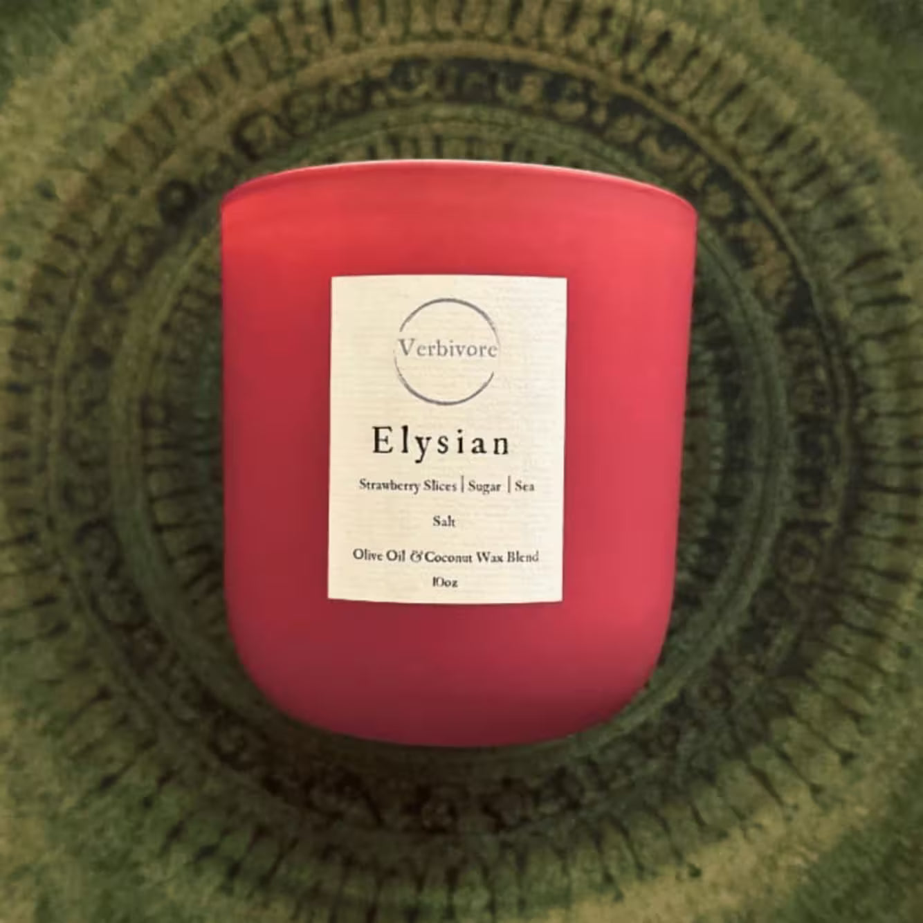 Red candle labeled 'Elysian' on a green textured surface