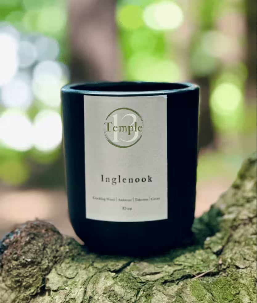 Black candle labeled 'Temple' on a tree stump with a blurred green forest background