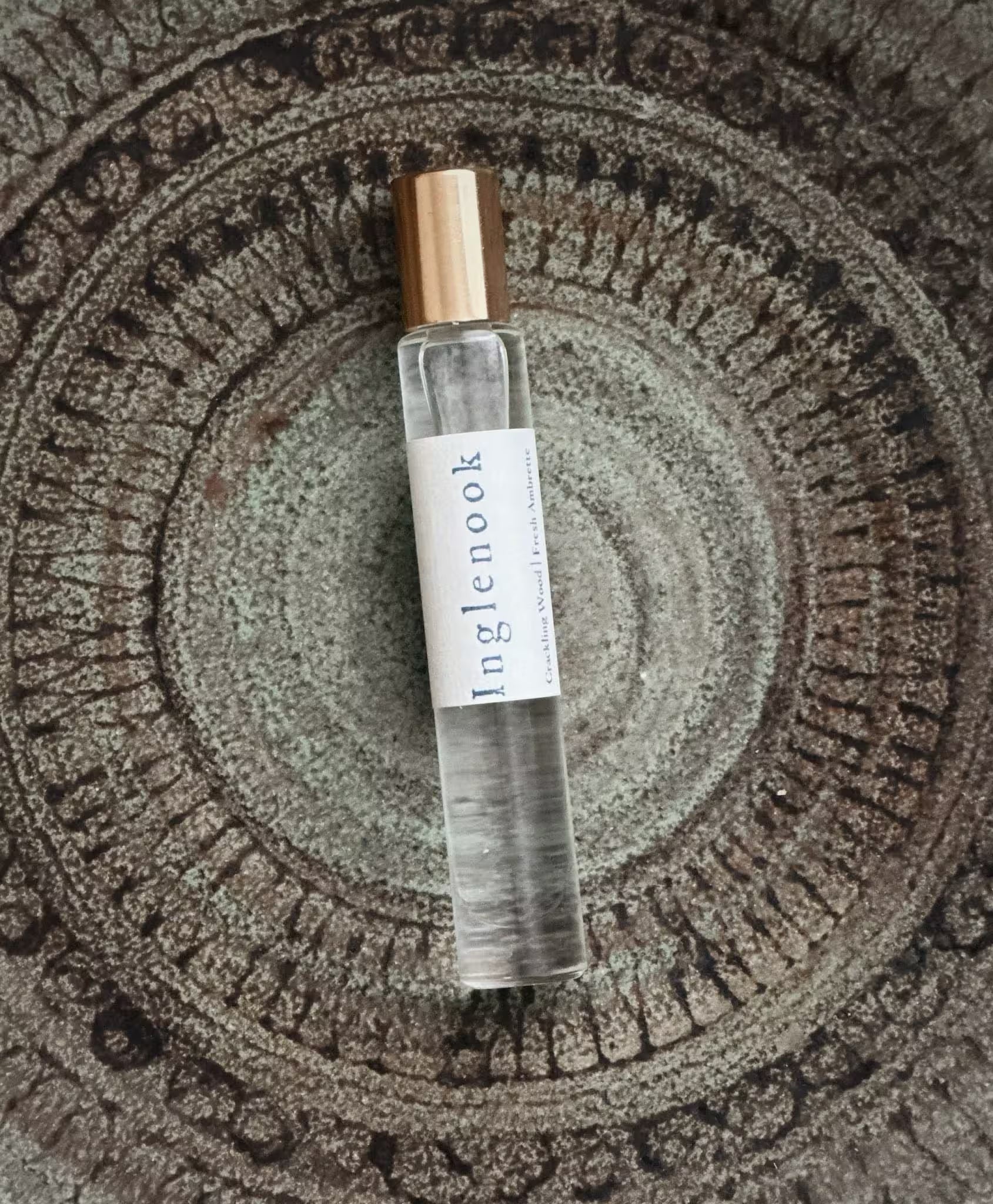 Small clear bottle with a gold cap on a textured stone surface, with the word 'Inglenook'.