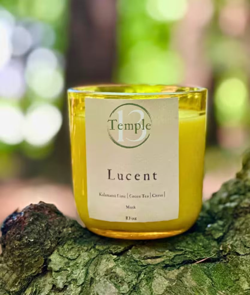 Yellow candle labeled 'Lucent' from 'Temple' on a tree stump with a blurred natural background