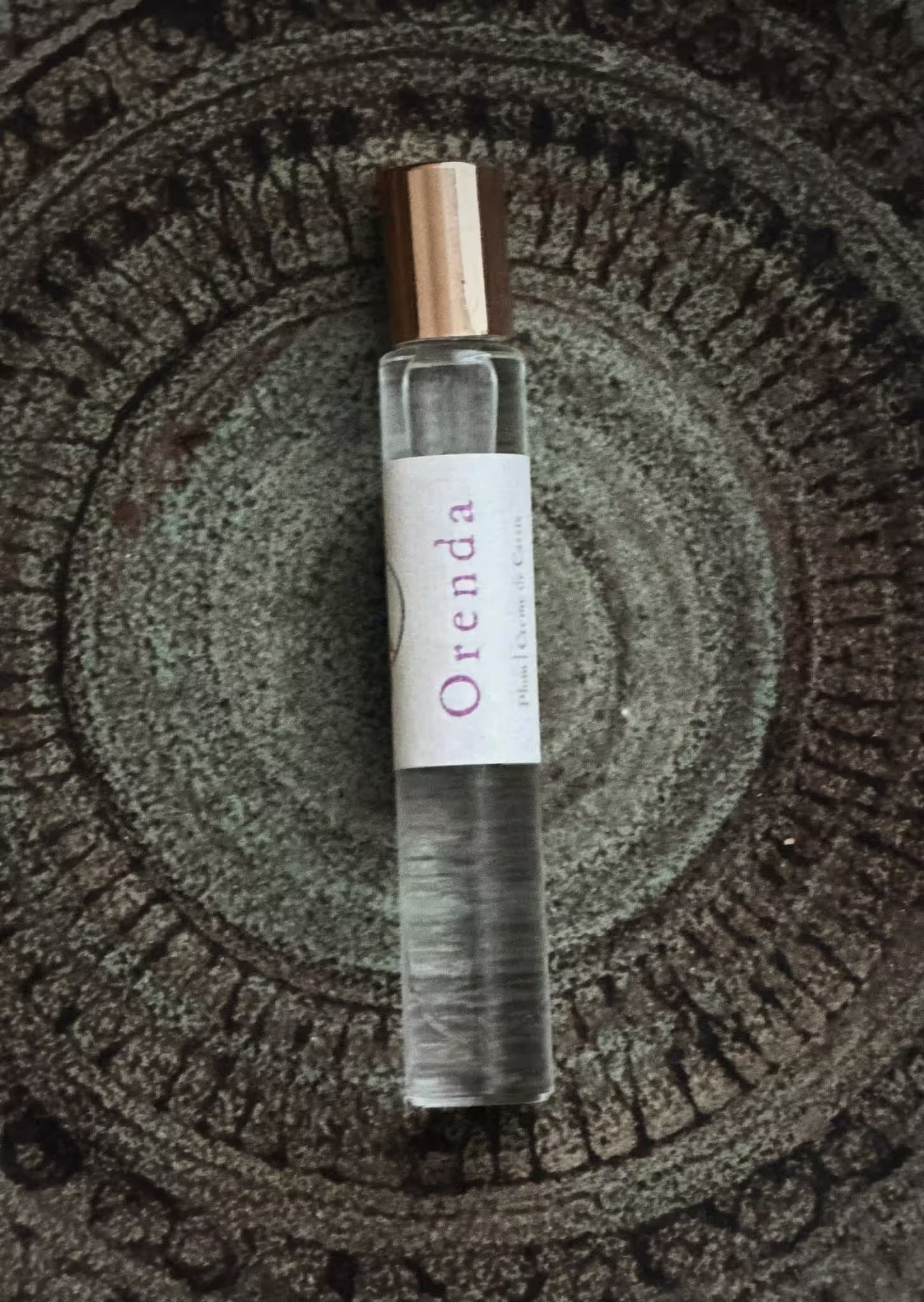 Small glass bottle with a gold cap on a textured surface with the word 'Orenda'.