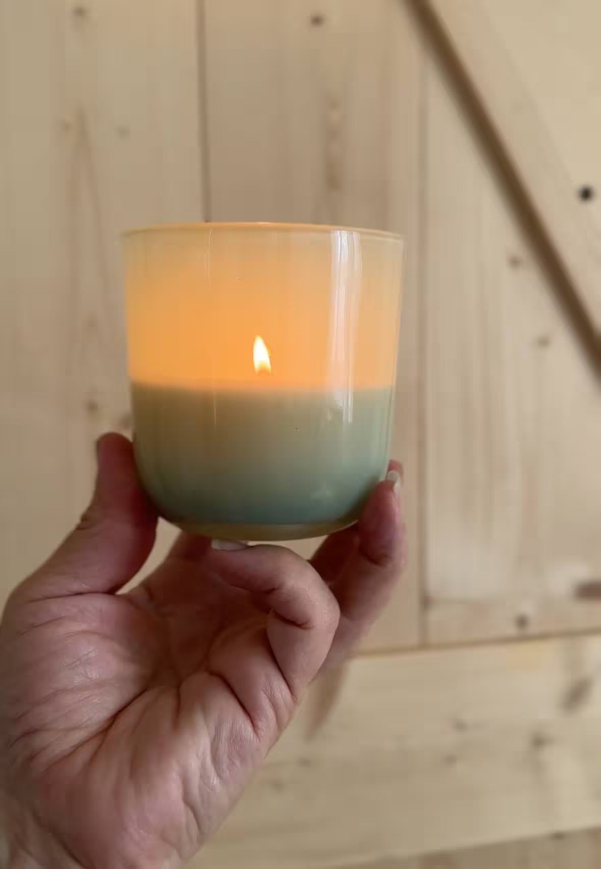 Hand holding a lit candle in a glass holder against a wooden background