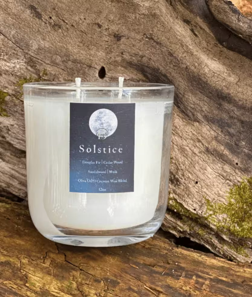 Candle in a glass jar with a 'Solstice' label on a log
