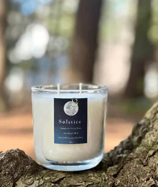 Candle labeled 'Solstice' on a tree stump with a blurred natural background