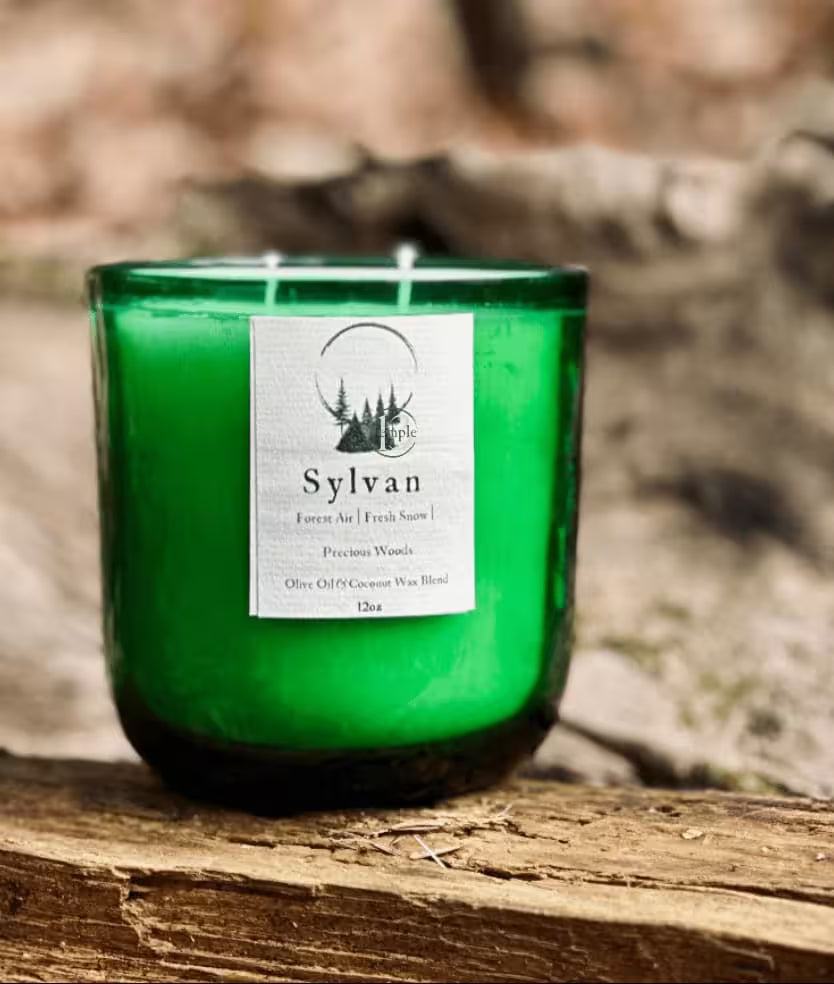 Green candle with a label on a log, blurred natural background