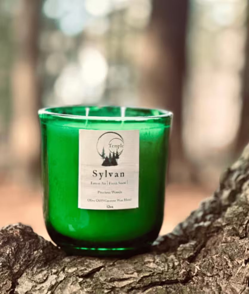 Green candle labeled 'Sylvan' on a tree stump with a forest background